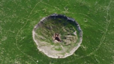 View of the funnel from a nuclear explosion, overgrown with green grass and a lake in the center of the funnel. There are many small craters around the large crater. large meteorite impact crater