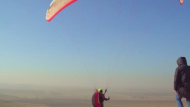 The pilot on the paraglider catches the tailwind, keeps the wing on top, trying to cherish.Above the paraglider there is a blue cloudless sky and autumn fields.
