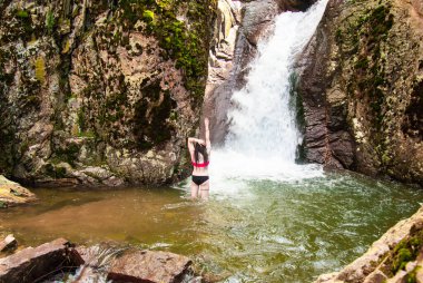 Mayolu bir kız dağ kayalıklarında şelalede mayo giyiyor. Göksel bir yer, su kayalıklardan aşağı akıyor.