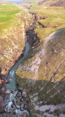 Kanyonun derinliklerinde turkuaz bir nehri olan dağlık kayalık bir bölge. Tepeler yeşil çimenler ve yemyeşil bahçelerle çevrili..