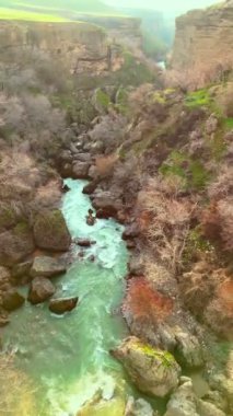 Kanyonun derinliklerinde turkuaz bir nehri olan dağlık kayalık bir bölge. Tepeler yeşil çimenler ve yemyeşil bahçelerle çevrili..