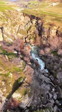 Kanyonun derinliklerinde turkuaz bir nehir bulunan dağlık kayalık bir bölge. Tepeler yeşil çimenler ve yemyeşil bahçelerle çevrili, büyüleyici doğal bir resim sunuyorlar..