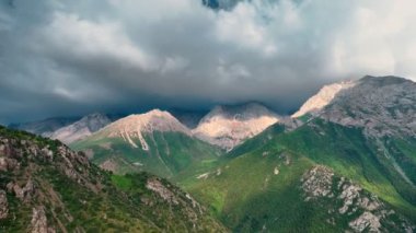 İnsansız hava aracı videosu, önünde yeşil tepeler olan tüylü bulutlarla çevrili görkemli dağları gösteriyor. Kamera pürüzsüz hareket ediyor, muhteşem bir doğal manzara ve sakin bir atmosfer ortaya çıkarıyor..