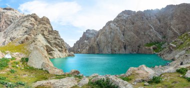 Görüntü, koyu kayalarla çevrili mavi bir gölü gösteriyor. Su berrak ve sakin. Çevredeki dağları yansıtıyor. Güney Kırgızistan 'ın büyülü ve muhteşem bir manzarasını yaratıyor..