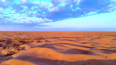 Mavi gökyüzünün altında kumullar, bulutlar, güneş doğarken drone 'lar tarafından yakalanır. Işık ve gölge, çöl manzarasının dokusunu ve derinliğini vurgular..