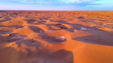 Gün batımı kumulları canlı turuncu ve mor tonlarda boyar. Havadan drone atışı sonsuz çölün muazzam boyutunu ve güzelliğini yakalar..