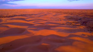 Gün batımı kumulları canlı turuncu ve mor tonlarda boyar. Havadan drone atışı sonsuz çölün muazzam boyutunu ve güzelliğini yakalar..