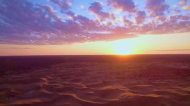 İnsansız hava aracı tarafından yakalanan çöl kumullarının üzerinde gün doğumu. Parlak gökyüzü ve kumdaki yumuşak gölgeler sakin ve görkemli bir doğal atmosfer yaratır..