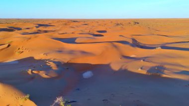 Mavi gökyüzünün altında kumullar, bulutlar, güneş doğarken drone 'lar tarafından yakalanır. Işık ve gölge, çöl manzarasının dokusunu ve derinliğini vurgular..