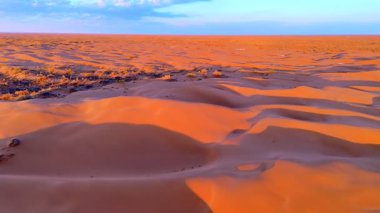 Gün batımı kumulları canlı turuncu ve mor tonlarda boyar. Havadan drone atışı sonsuz çölün muazzam boyutunu ve güzelliğini yakalar..