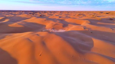 Gün batımı kumulları canlı turuncu ve mor tonlarda boyar. Havadan drone atışı sonsuz çölün muazzam boyutunu ve güzelliğini yakalar..