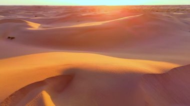 Zıt dokulara sahip dalgalı kum tepeciklerinin havadan görünüşü. Sabah ışığı yumuşak gölgeler bırakır, doğal çöl şekillerini ortaya çıkarır..