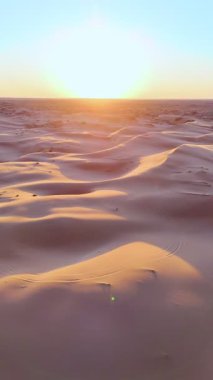 İnsansız hava aracı tarafından ele geçirilen kum tepelerinin üzerinde şafak vakti. Yumuşak ışık kumun altın dalgalarını boyar, sıcaklığı ve sonsuzluğu anımsatır..