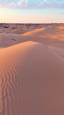 Güneşin doğuşunda ya da batışında kum tepelerinin drone üstgeçidi. Yumuşak ışık, pürüzsüz çöl şekilleri ve berrak gökyüzü dingin ve huzurlu bir hava yaratır..