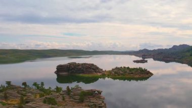 Bulut yansımalı sakin göl ve yeşil tepelere karşı kayalık adalar
