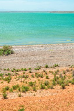 Kırmızı yamaçlar ve göl kıyısının yanındaki yeşil bozkır zıt bir manzara yaratır.