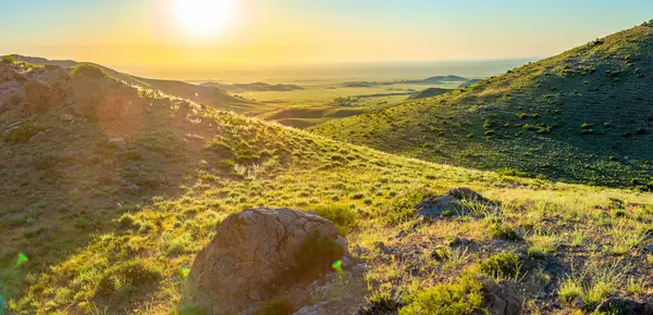 Yeşil tepelerin ve vadilerin üzerinde gün batımı, altın güneş ışığıyla aydınlanıyor.