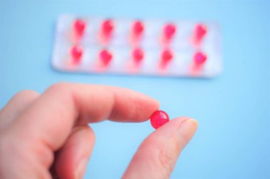 Soluk mavi arka planda insan parmaklarında yuvarlak kırmızı vitaminler.