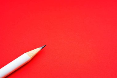 White pencil on red paper table. Top view, copy space.
