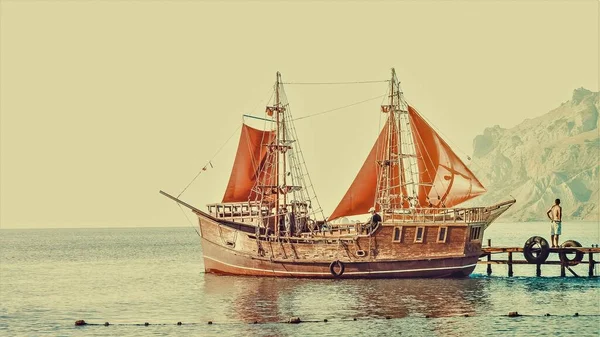 Wooden ship with red sails at the sea moorage.