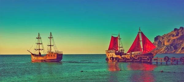 Two old wooden ships with red sails on the sea pier.