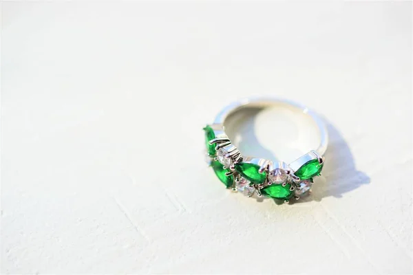 Platinum ring with crystals and emerald stones on a white stone table.