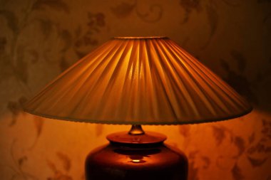 Pleating lampshade with warm light in dark room, closeup clipart