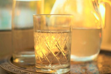 Glass of water and jug of water in a tray on the sunny windowsill