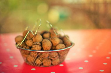 Kırmızı masa örtüsünde beyaz noktalı ceviz dolu bir ağ kasesi..