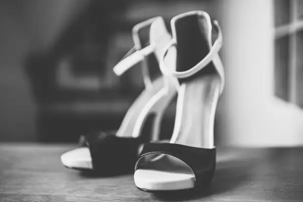 Black and white heeled sandals stand on the wooden floor.