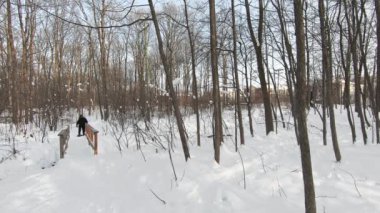 Öndeki adam ormanda kar ayakkabısı giyiyor, karla kaplı bir patikada ve kışın küçük bir köprüyü geçiyor.