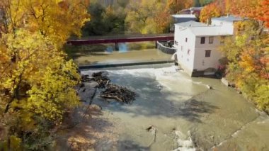 St-Eustache 'deki Legare Değirmeni' nin yanında geriye doğru uçan hava aracı videosu, nehrin üzerinde ve şelalenin üzerinde sonbaharın renklerini gösteriyor.