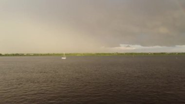 Fırtınadan sonra suda yüzen bir yelkenlinin videosu dramatik bulutlar ve etrafta uçuşan martılarla