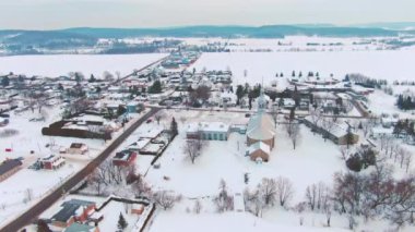 Drone yüksek irtifada ateş etti, karlı mezarlığın üzerinden geriye doğru uçtu ve St-Benoit de Mirabel köyünü açığa çıkardı.