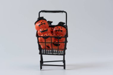 Beyaz arka planda alışveriş arabasında şapka takan şirin Cadılar Bayramı balkabakları..