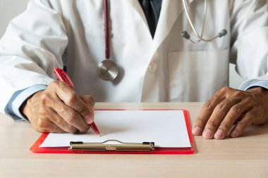 Üniformalı ve steteskoplu bir doktor, tıp bürosunda kağıt üzerine yazı yazıyor..