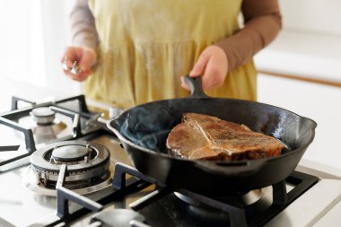 Gaz ocağında demir tavada biftek yakan bir kadın. Buhar yükseliyor. Yemek pişirmek, ızgara yapmak ve gurme yemek temaları için mükemmel..