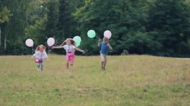 Ellerinde balonlarla parktaki yeşil çimenler boyunca koşan neşeli çocuklar. Oğlan ve kızlar eğleniyor..