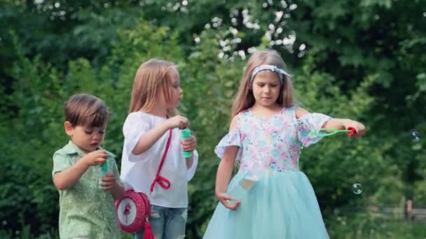 子供たちは公園でシャボン玉で遊ぶ 木の近くの自然の中で小さな男の子と2人の女の子 — ストック動画