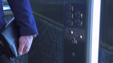 Asansördeki işadamı parmağıyla zemin düğmesine basıyor. İş merkezindeki asansör kapısını kapatıyorum. Çantalı takım elbiseli bir adam..