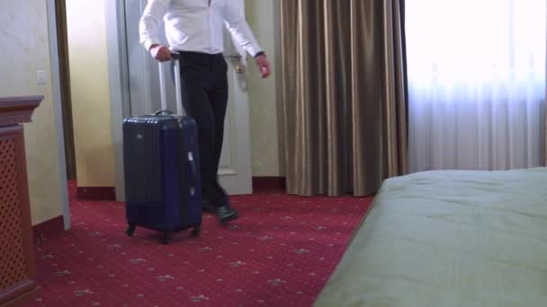 ズボン姿の男と白いシャツを着た男がホテルの部屋にチェックインする 車で移動するためのプラスチック製のスーツケースがベッドの上に置かれ ロックを開きます — ストック動画