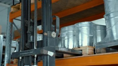 Metal rehberli elektrikli forklift endüstriyel bir depodaki bir raf dolusu ürünü kaldırır. Metal kaplarla paketlerin depolanması.