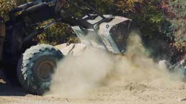 Granit ocağındaki eski paslı kazıcı kovadan kum döker. Tekerleklerin altındaki toz ve taşlar. İş yükleniyor.