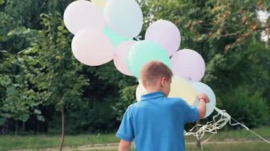 Elinde balonlar olan bir çocuk. Oğlan yaz parkında oynuyor. Kendi etrafında dönüyor..