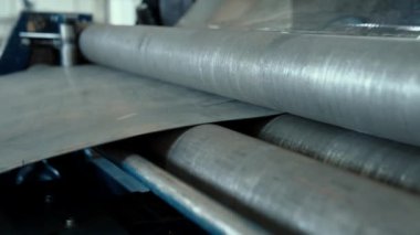 Metal levha iki dönen tekerlek arasında bir makinede bükülür. Bir endüstriyel şirkette metal ürünleri üretimi.