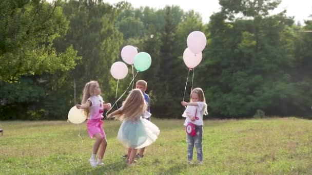ドレスを着た女の子と風船を手にして公園の芝生の上を旋回し ジャンプしています 子供たちは夏に屋外で遊ぶ スローモーション — ストック動画