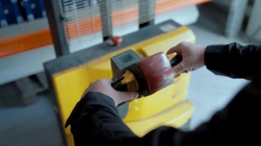 Ellerini hidrolik istifleyicinin kontrol koluna koy. Bir işçi depoda yük taşır. Yakın plan..