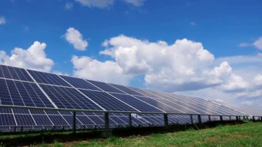 Yeşil çimen tarlasında kutuplara monte edilmiş uzun güneş panelleri. Güneş enerjisi santrali. Yumuşak kamera hareketi.