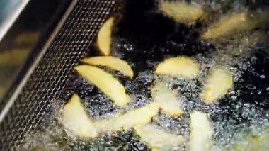 Patates kızartmaları mutfakta büyük bir konteynırda kaynar yağda kızartılır. Yağ içinde patates parçaları. Ağır çekimde yakın çekim.