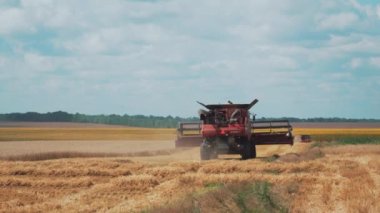 VINNYTSIA, UKRAINE - 19 Temmuz 2020: Kırmızı hasatçılar çim biçme tarlasında ilerliyorlar. Mısır gevreği hasadı. Bulutlu mavi gökyüzünün arka planında sarı bir buğday tarlası.